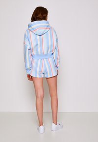 Sudadera a rayas azul claro con líneas de colores del arcoíris, combinada con pantalones cortos a juego. La tela parece suave, con un corte relajado y acentos de canalé.
