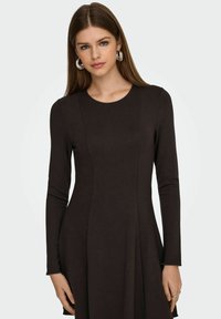 Abito nero a maniche lunghe, corpetto aderente, gonna a campana, texture a coste, scollatura rotonda, design semplice, indossato con grandi orecchini a cerchio d'argento.