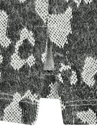 Schwarz-weißer Strickstoff mit geometrischem Muster, der eine fuzzy Textur und sichtbare Fäden aufweist, und einen leicht ausgefransten Rand zeigt.