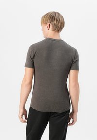 Short-sleeve, fitted shirt in dark gray ribbed fabric. Features a crew neckline and a smooth texture, worn with black corduroy pants.