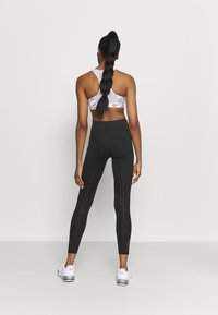 Leggings neri a vita alta con pannelli testurizzati, abbinati a un reggiseno sportivo con motivo e sneaker bianche, visti da dietro.