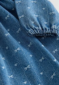 Tessuto in denim di colore azzurro chiaro con motivi a fiocco bianchi. Il materiale presenta una trama texturizzata e dettagli in elastico arricciato.