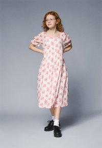 Floral print, knee-length dress in light pink with puffed sleeves. Black lace-up shoes, white socks visible. Smooth fabric texture.