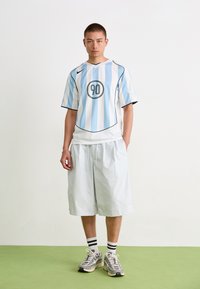 Blå og hvitstripet kortermet jersey med et rundt merke, sammen med lyse shorts og sneakers med grå, hvite og svarte detaljer.