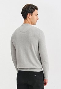 Szary sweter dziany z okrągłym dekoltem i prążkowanymi mankietami. Posiada krótki krój i gładką teksturę, noszony na ciemnych spodniach.