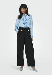 Blusa azzurro chiaro con dettagli arricciati sul davanti, maniche lunghe; abbinata a pantaloni neri a gamba larga a vita alta; completata con tacchi azzurro chiaro.