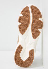 Sko sula med en texturerad brun gummimönster och vit mellansula, som visar en böjd design för grepp och stöd.