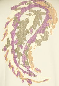 T-shirt med et tekstureret grafisk design i lilla, grønne og orange nuancer på en lys cremet baggrund, med abstrakte, bølgede mønstre.