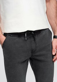 Pantalones jogger de un gris oscuro con cintura elástica, que cuentan con un cordón negro y bolsillos laterales. La tela tiene un acabado suave.