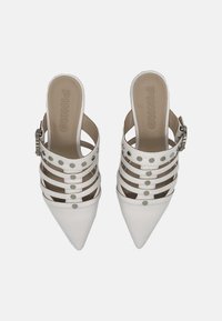 Scarpe slingback bianche a punta con più cinturini, borchie argentate e un accento a fibbia. Materiale in pelle liscia, suola piatta.