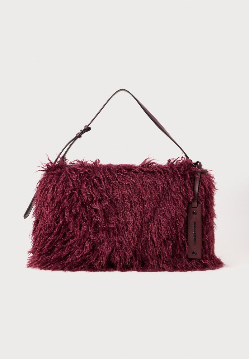 Burgunderfarbene Handtasche mit flauschiger Textur, ausgestattet mit einem kurzen Ledertragegurt und einem seitlichen Etikett für die Markenkennzeichnung. Weiches, strubbeliges Materialdesign.