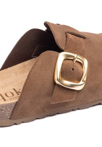 Sandal en suède marron à glissière avec une grande boucle carrée dorée, semelle intérieure texturée avec une base en liège, et semelle extérieure en caoutchouc flexible.