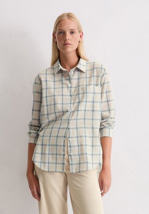 Een button-up shirt gemaakt van lichte stof, met een lichtbeige achtergrond en een blauwgroene vierkante patroon. Lange mouwen, met een zakdetail.