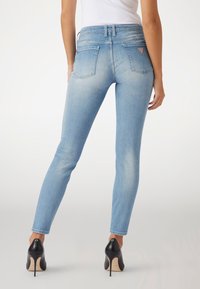 Jeans ajustados de mezclilla azul claro con una textura suave, diseño de cinco bolsillos y un pequeño logo en el bolsillo trasero. Combina con tacones altos.