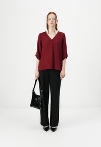 Top bordeaux con scollo a V e maniche corte, abbinato a pantaloni neri a gamba larga. Accessoriato con una borsa in pelle nera e scarpe a punta.