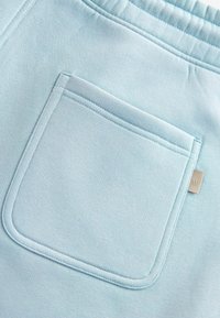 Pantaloni della tuta azzurro chiaro con una tasca posteriore singola con contorno cucito e un piccolo logo metallico. Tessuto liscio e morbido.