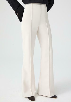 I pantaloni bianchi a gamba larga presentano un design sartoriale con dettagli delle cuciture verticali, un tessuto liscio e tacchi a punta neri.