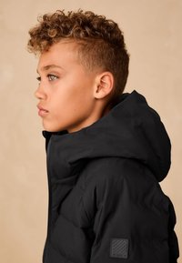 Schwarze Steppjacke mit hohem Kragen und Kapuze; glatte Textur und Steppdetail; verfügt über ein kleines Markenlogo am Ärmel.