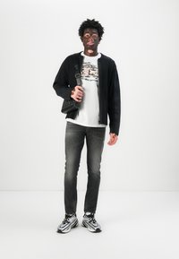 Čierny rebrovaný cardigan, biele tričko s grafikou, poškodené šedé džínsy a čierno-strieborné tenisky. Doplnok: malá čierna crossbody taška.
