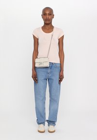 Ljusrosa tajt t-shirt med logotypdesign, ihopparad med lösa blå jeans och beige sneakers; en liten grå crossbody-väska med kedjeslår.