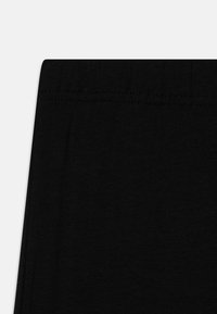 Schwarzer Baumwollstoff mit glatter Textur, ausgestattet mit einem breiten, elastischen Bund und dezenten Nähten nahe der oberen Kante.