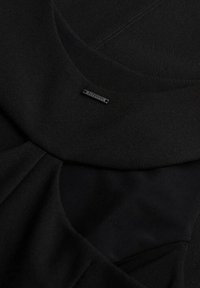 Czarna teksturowana tkanina z okrągłym dekoltem i małą metalową metką marki Superdry przymocowaną blisko kołnierza.