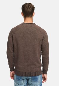 Pull en tricot marron avec un col et un ourlet côtelés, présentant un motif texturé. Porté avec un jean bleu clair, montré de dos.