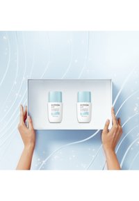Produits de soins Biotherm dans une boîte blanche, avec deux bouteilles blanches à capuchons bleu clair sur un fond bleu doux.