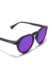 Ochelari de soare octagonali negri cu lentile violet și finisaj mat. Prezintă brațe de temple unghiulare și brandingul "HAWKERS" pe lateral.