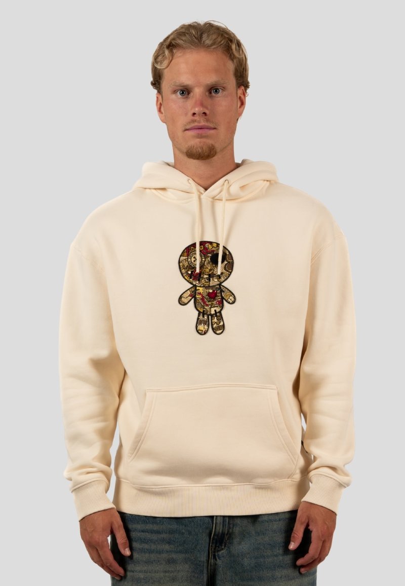 Cream hoodie featuring a textured, embroidered doll design in gold and red. It has a front pocket and ribbed cuffs and hem.