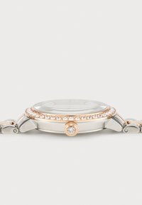 Montre ronde avec un boîtier en acier inoxydable argenté, des accents en or rose et une lunette ornée de cristaux. Dispose d'un cadran texturé et d'un fermoir.