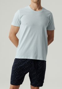 Jasnoniebieska koszulka z krótkim rękawem i okrągłym dekoltem. Połączona z granatowymi szortami z rozproszonym niebieskim prostokątnym wzorem i regulowanym pasem na sznurki.