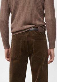 Pantalones de pana marrón con un corte recto, que cuentan con dos bolsillos traseros y un suéter marrón texturizado. Cintura visible.