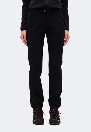 Un mannequin porte un pantalon noir à jambes droites avec un bouton à la taille et des chaussures de randonnée noires à lacets rouges, sur un fond uni.