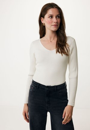 Top bianco a maniche lunghe e righe con scollo a V, abbinato a jeans neri a vita alta. Il tessuto è liscio e presenta una silhouette aderente.
