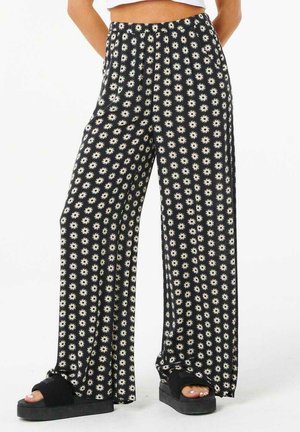 Pantaloni neri a gamba larga con un motivo floreale bianco. Realizzati in tessuto morbido con una vestibilità rilassata e una cintura elastica. Sandali neri con suola spessa.