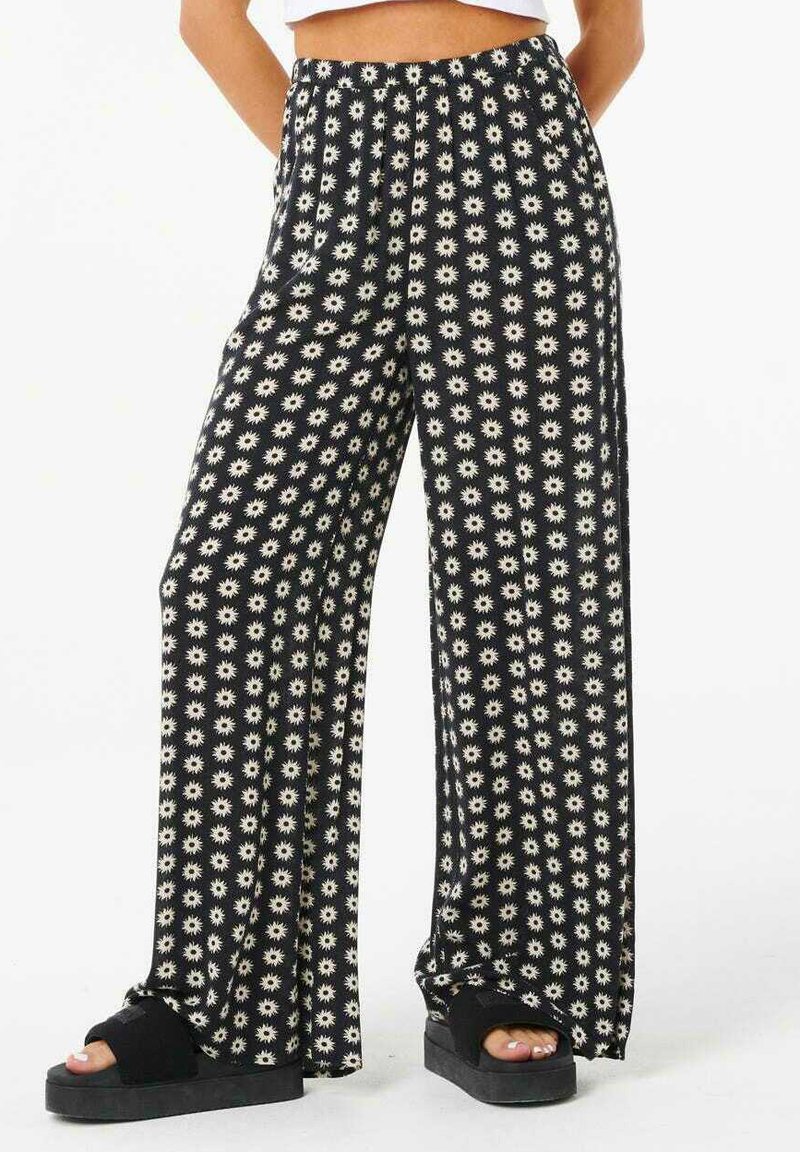 Pantaloni neri a gamba larga con un motivo floreale bianco. Realizzati in tessuto morbido con una vestibilità rilassata e una cintura elastica. Sandali neri con suola spessa.