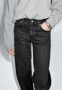 Czarne dżinsy o prostym kroju, z przednimi kieszeniami i srebrnymi guzikami. W zestawie z szarym swetrem.