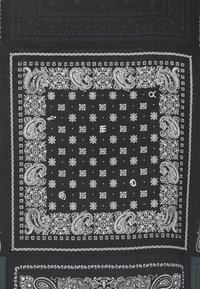 Bandana nera con motivi paisley bianchi, motivi floreali e design a griglia. Il tessuto è testurizzato, con bordi e dettagli intricati.
