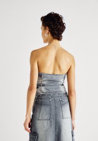 Vestido strapless de denim gris con un corpiño ajustado, bolsillos traseros y detalles de ojetes. Presenta una forma estructurada y una textura sutil.