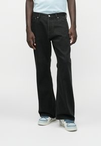 Melnas denim bikses ar taisna piegriezuma dizainu, kas ietver klasisku piecu kabatu stilu un baltu šuvumu. Apvienotas ar gaiši zilām sporta kurpēm.