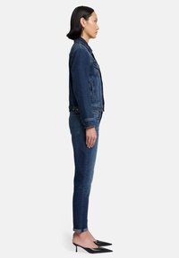 Giacca di jeans blu scuro con colletto classico, tasche frontali e chiusura a bottoni. Abbinata a jeans skinny scuri e décolleté nere.
