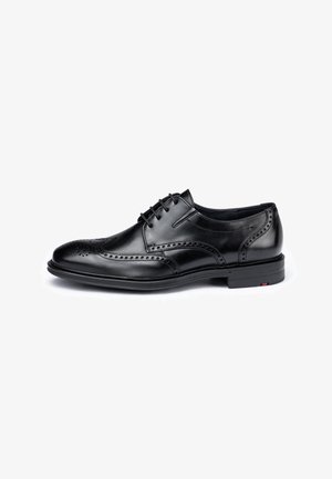 Czarny męski elegancki but ze skóry z ozdobami typu wingtip brogue i sznurowadłami, przedstawiony z profilu na białym tle.