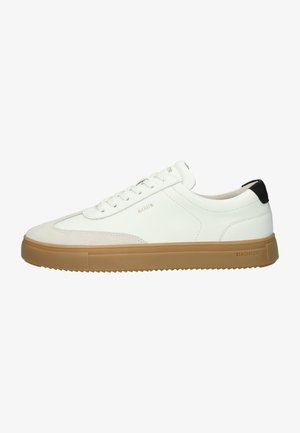 Witte leren sneakers hebben een gestructureerde suede voorkant, een beige rubberen zool met ribbels en zwarte hielaccenten met subtiele branding.