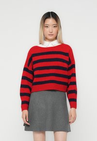 Rød og marineblå stripet genser med en cropped design, vide ermer og ribbet kant, sett sammen med et grått svingeskjørt. Glatt tekstur.