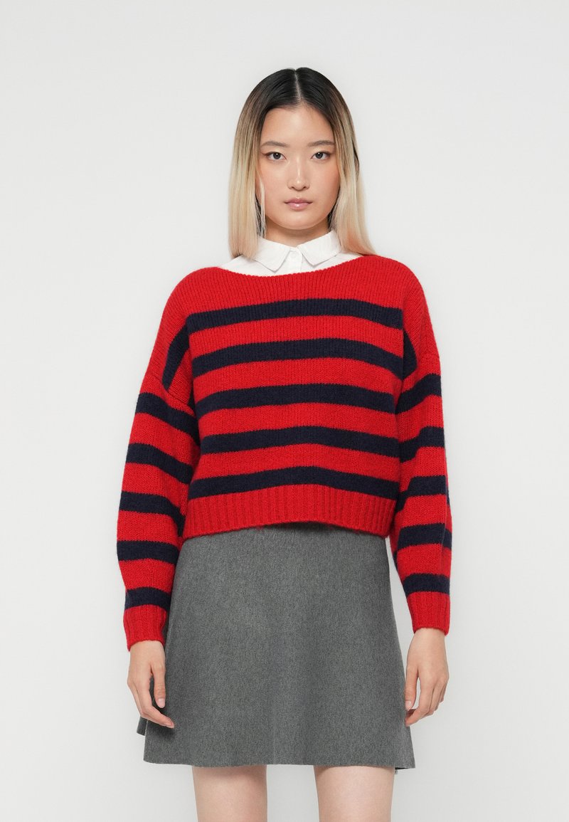 Rød og marineblå stripet genser med en cropped design, vide ermer og ribbet kant, sett sammen med et grått svingeskjørt. Glatt tekstur.