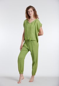 Completo in lino verde a due pezzi che presenta una blusa morbida a maniche corte con scollo a V e nappine, abbinata a pantaloni con polsini elasticizzati.