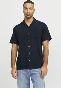Marineblauw kortetermijnshirt met een gestructureerde stof, knoopsluiting aan de voorkant en een borstzak. Voorzien van witte knopen en een klein logo op de zak.