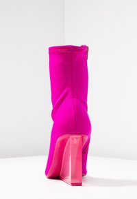 Bottines fuchsia en matériau lisse et extensible, avec un talon bloc transparent et un détail de fermeture éclair sur le côté.