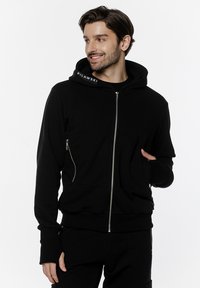 Czarny rozpinany hoodie wykonany z miękkiego materiału, z kieszenią kangurką, srebrnymi detalami zamka błyskawicznego oraz logotypem wzdłuż kaptura.